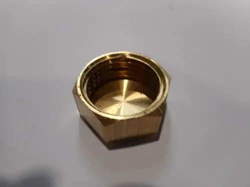 Brass nut, likely from Remeha, featuring internal threading and a hexagonal shape, placed on a light-colored surface.